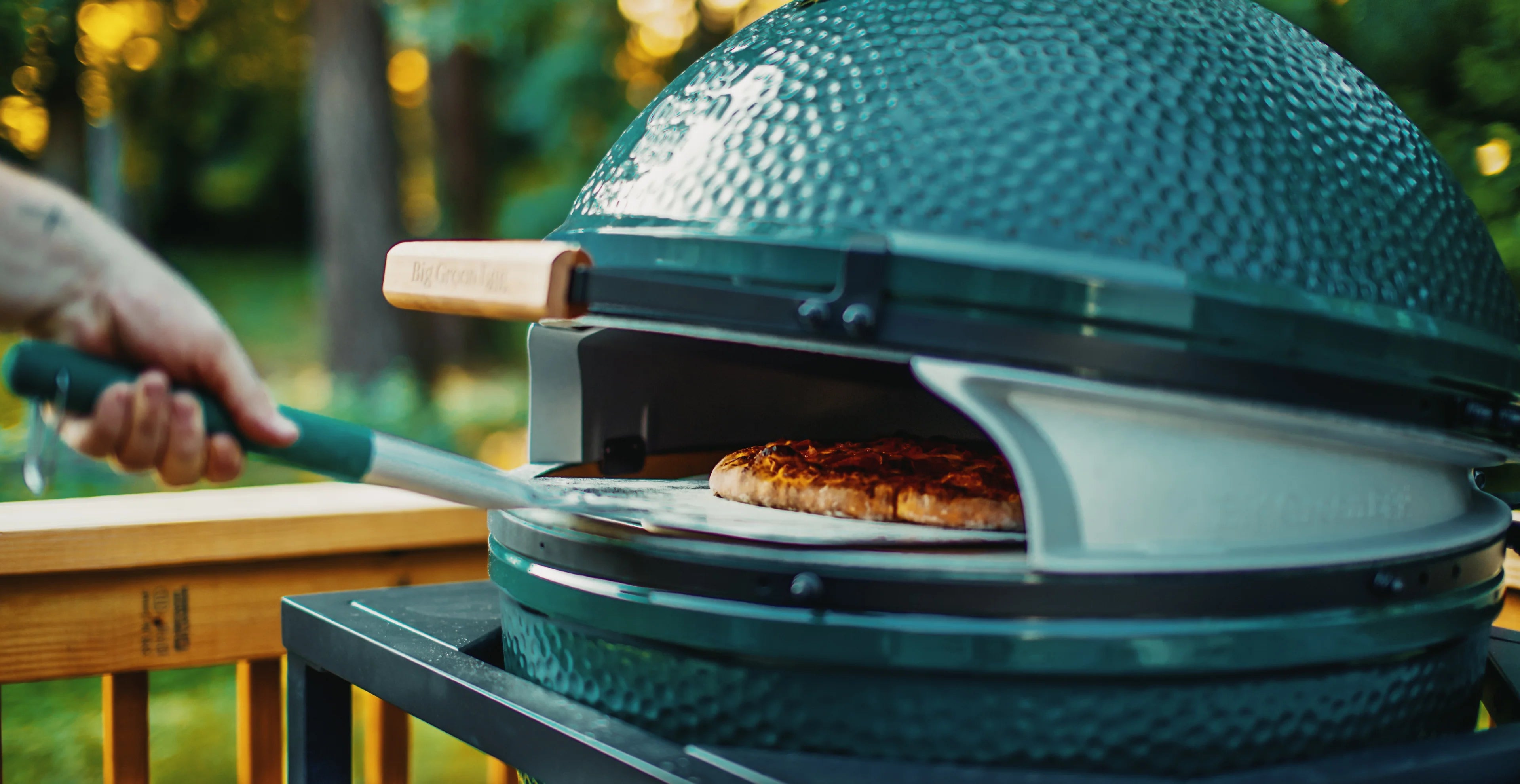 Big Green Egg outdoor pizza oven with a pizza being cooked on a grill