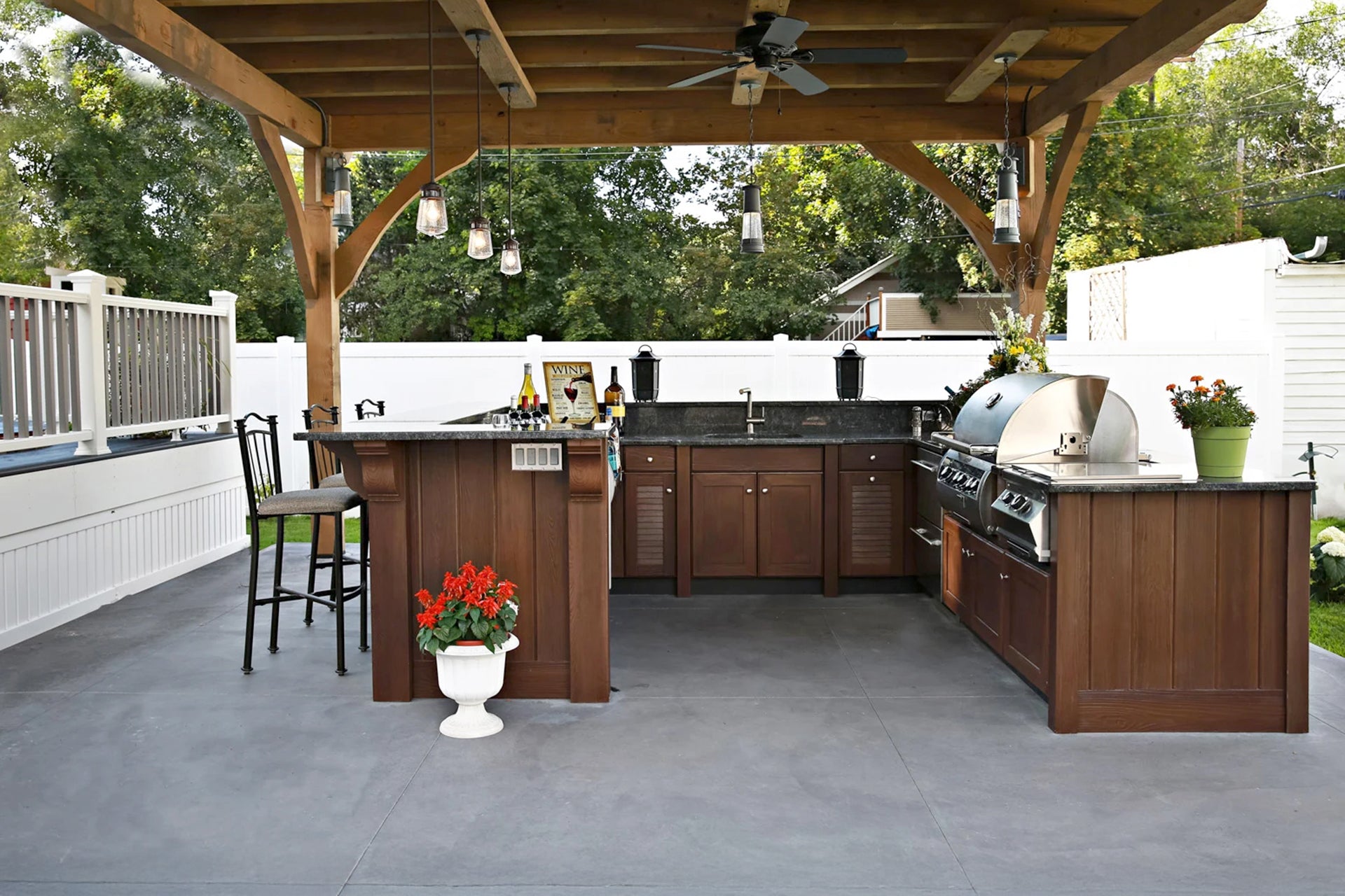 Outdoor kitchen with wooden cabinets, grill, and bar area on a patio.