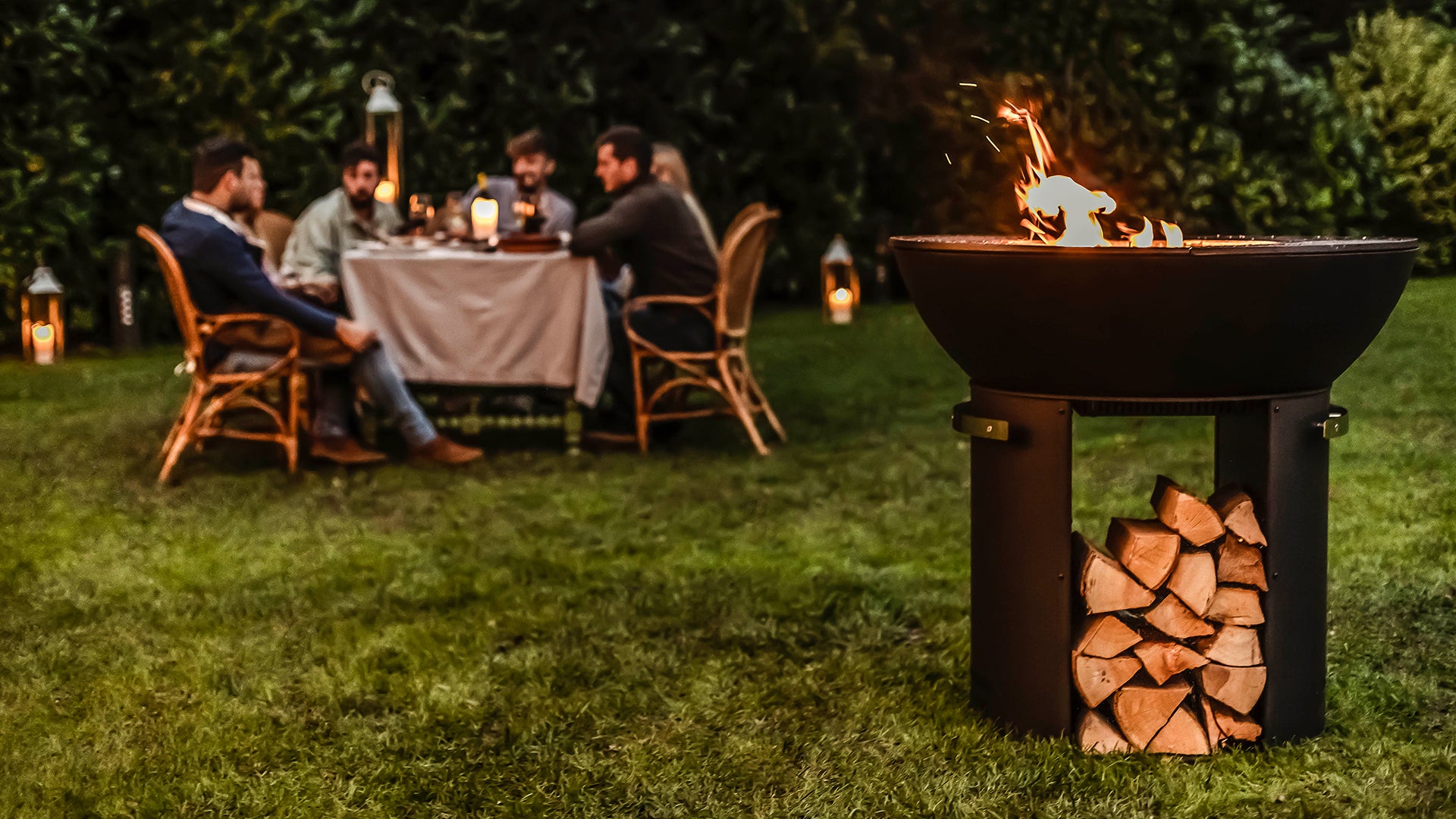 People sitting at a table in the background with a fire pit in the foreground.